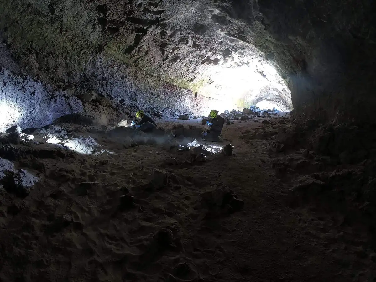 Researchers in helmets and gloves sampling the floor of a dark cave